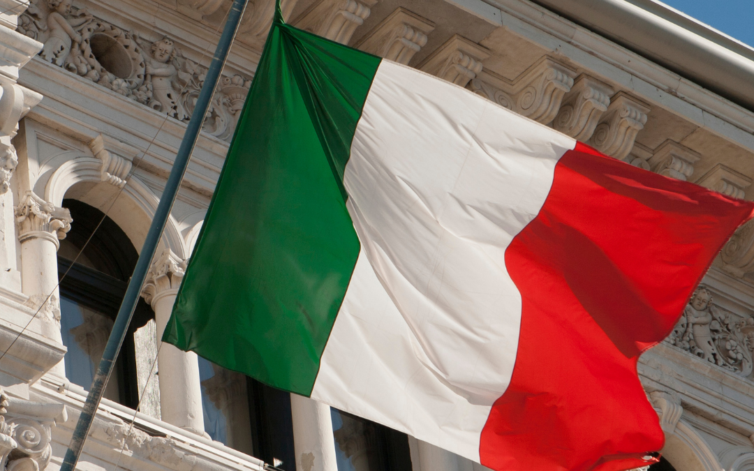 foto de uma bandeira italiana com um edifício antigo atrás simbolizando a unificação da itália.