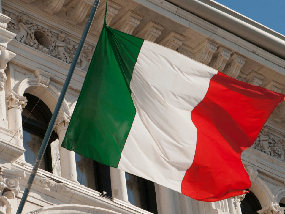 foto de uma bandeira italiana com um edifício antigo atrás simbolizando a unificação da itália.