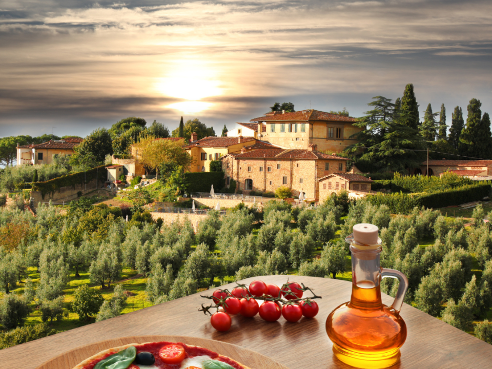 foto de uma paisagem diante de uma mesa com uma pizza, azeite e tomates em cima.